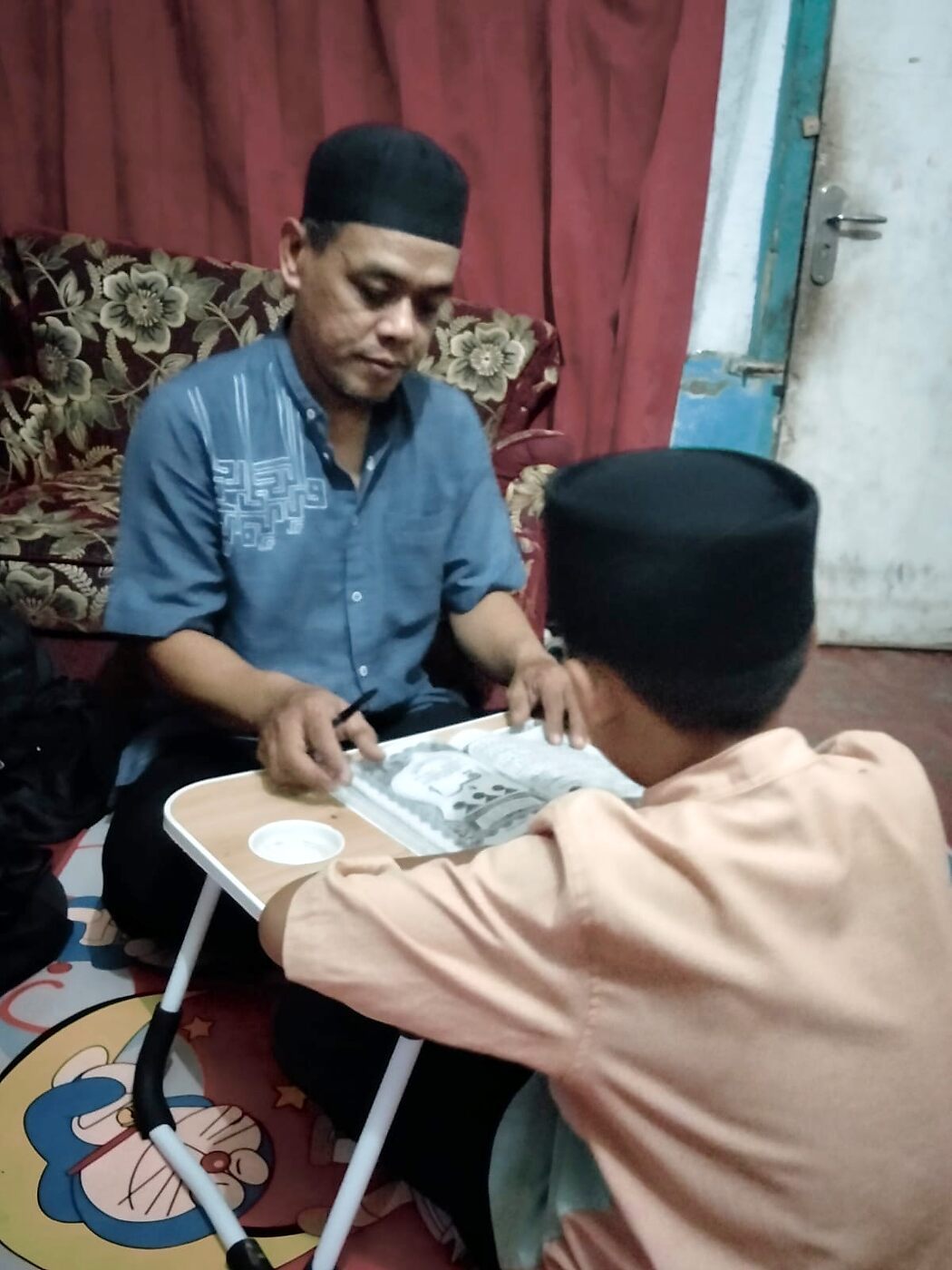 Guru Ngaji laki-laki mendampingi anak belajar membaca Al-Qur'an di rumah